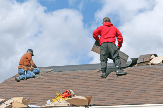 Two men replacing shingles on a house roof