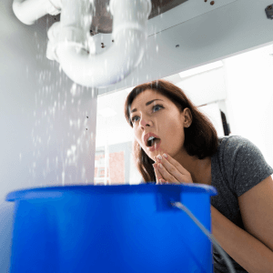 woman looks under sink at leaking pipe- signs of water damage