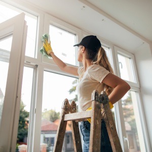 woman deep clean windows on ladder